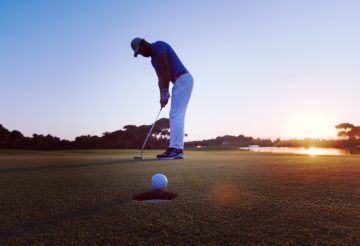 golfer hitting ball shot with driver on golf course at beautiful sunset in background