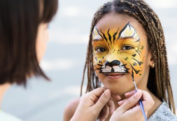 Cute little tiger. African-american girl getting face painting outdoors, having fun, copy space